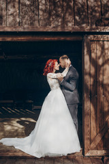 rustic wedding couple posing and hugging in sunlight at background of wooden wall in country barn....
