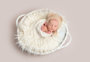 Newborn baby in funny bonnet napping in basket