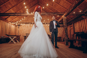 rustic wedding couple dancing under retro bulbs lights in wooden barn. space for text. newlyweds embracing, sensual romantic moment. stylish groom and happy bride posing