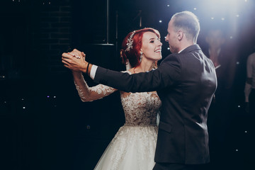 happy bride and stylish groom dancing at wedding reception. gorgeous wedding couple performing ...