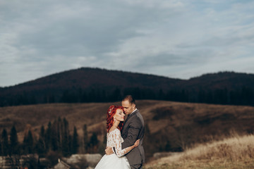 happy stylish bride and groom hugging in mountains in sunset light. gorgeous boho newlywed couple embracing, true feelings. emotional romantic moment. space for text