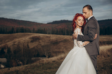 Fototapeta na wymiar happy stylish bride and groom hugging in mountains in sunset light. gorgeous boho newlywed couple embracing, true feelings. emotional romantic moment. space for text