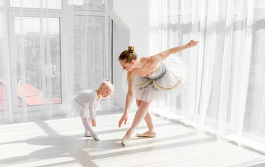 Obraz premium Young gorgeous ballerina with her little daughter dancing in studio