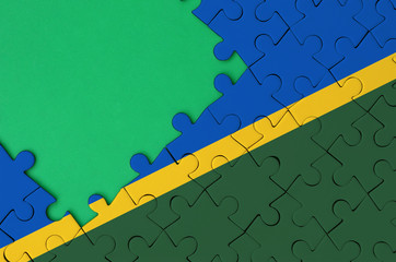 Solomon Islands flag  is depicted on a completed jigsaw puzzle with free green copy space on the...
