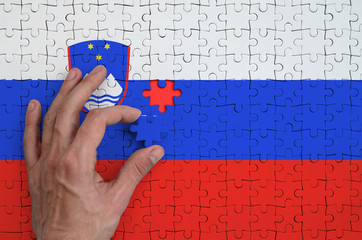 Slovenia flag  is depicted on a puzzle, which the man's hand completes to fold