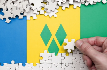 Saint Vincent and the Grenadines flag  is depicted on a table on which the human hand folds a...