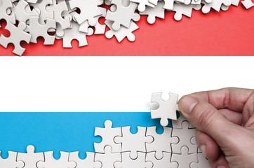 Luxembourg flag  is depicted on a table on which the human hand folds a puzzle of white color