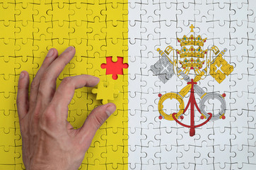 Vatican City State flag  is depicted on a puzzle, which the man's hand completes to fold