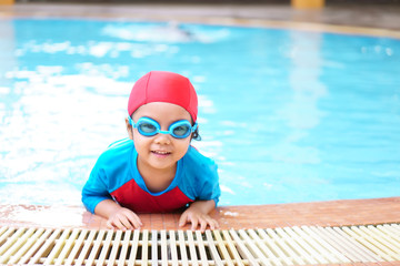 Asian children cute or kid girl wear swimming suit and goggles on swimming pool and smile with...