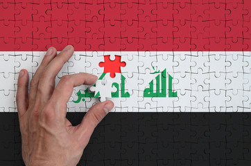 Iraq flag  is depicted on a puzzle, which the man's hand completes to fold
