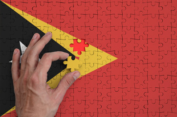 Timor Leste flag  is depicted on a puzzle, which the man's hand completes to fold
