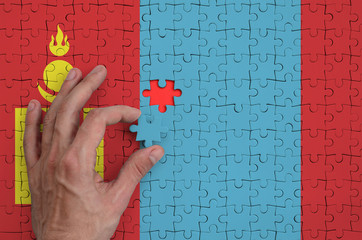 Mongolia flag  is depicted on a puzzle, which the man's hand completes to fold