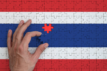 Thailand flag  is depicted on a puzzle, which the man's hand completes to fold