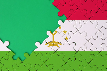 Tajikistan flag  is depicted on a completed jigsaw puzzle with free green copy space on the left...