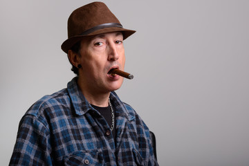 Studio shot of mature gangster man smoking cigar