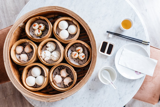 Top view of Dim sum set: Barbecued pork bun, Shrimp dumpling, Sweet cream buns, Shrimp shumai topping with goji berry served in steamer baskets with plate, chopsticks, sour sauce and hot tea.