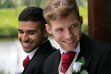 Gay couple of grooms pose for photographs by a lake on their wedding day