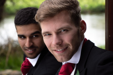 Gay couple of grooms pose for photographs by a lake on their wedding day