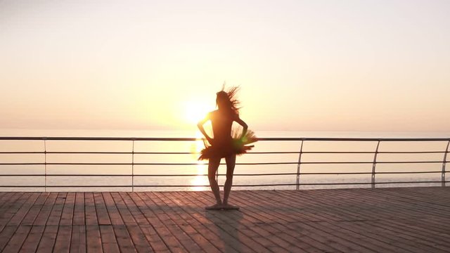 Young, tender ballet dancer practicing near the sea ocean. Jumping up on the spot. In dark tutu and pointe. Backside view. Morning