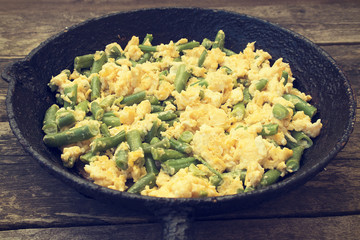 Green beans fried with eggs beautiful in an old frying pan on a wooden background, rustic style