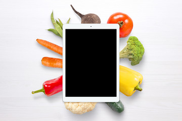 Blank tablet for mockup. Vegetables in background on white wooden table.