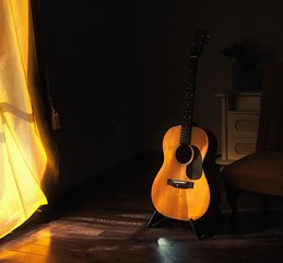 Acoustic Spanish guitar on a stand in the moody shadows of a dark room with bright light coming in...