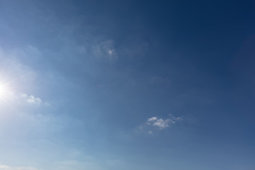 Blauer Himmel mit Sonne am Rand und Wolken