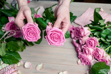Graceful female hands collect a bouquet of pink roses. Florist at work