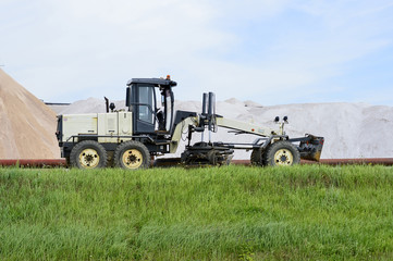 The grader is at the dam with pipeline in the background of mine. Side view. Foreground green grass