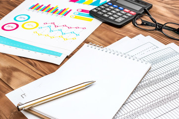 Blank notepad with financial documents, calculator and glasses on the wooden table. Businessman's workplace. Business concept.