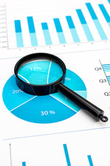 Magnifying glass on business graphs and charts. Financial concept.