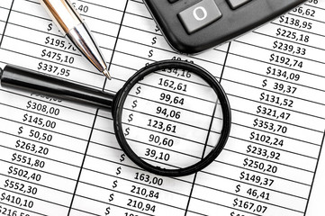 Magnifying glass with pen and calculator on the document with financial data. Top view.