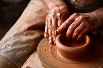 Close-up hands of a male potter in apron molds bowl from clay, selective focus