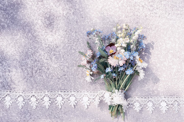 forget me not, lily of the valley and wild flowers bouquet laying on an old rustic silver table in the lace frame with copy space for your greeting text.
