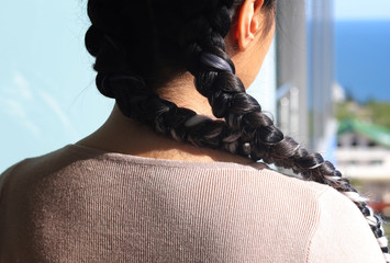 two braids, a haircut close-up of her own hair, details of the hairstyle, hairdressing art on her...