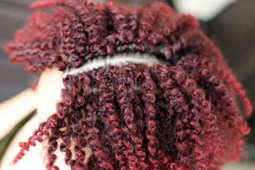 African curls made of artificial material, red synthetic curly hair braided on the girl close-up hairstyles on a light background