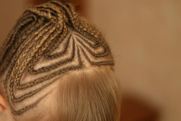 little girl with thin pigtails on the head, blonde hair, pigtails are gathered in the tail, close-up of an African hairstyle for beauty salons