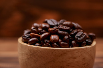 Wooden bowl with roasted coffee beans on rustic background.