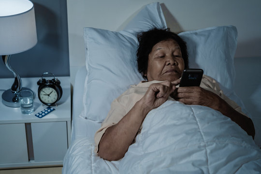 senior woman using mobile phone on bed at night