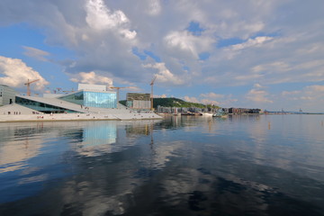 Widok budynku opery w Oslo, Norwegia, z przeciwnego brzegu zatoki morza, promenady z nowymi budynkami na brzegu, słonecznie, malownicze chmury na niebie - obrazy, fototapety, plakaty