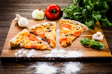 Slices of pizza and vegetables on wooden table