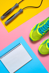 Sports equipment with shoes, skipping rope and blank notebook on colorful background, copy space. Top view, flat lay. Sport, fitness concept, healthy lifestyle