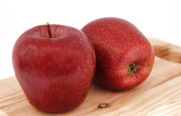 Dos manzanas rojas sobre tabla de madera, en fondo blanco 