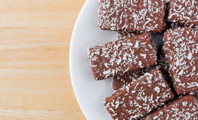 Top close view of chocolate wafer with coconut flakes cookies on a white plate atop a wood table.