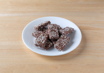 Chocolate wafer with coconut flakes cookies on a white plate atop a wood table.
