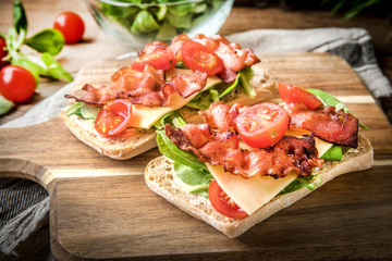 Ciabatta sandwich with arugula salad, bacon and yellow cheese.
