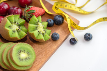 Closed up on fresh green kiwi, blueberries, strawberries and measurement tape on white background. Healthy and dietary concept.
