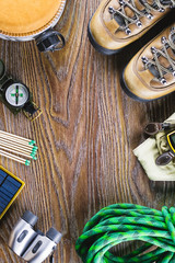Hiking or travel equipment with boots, compass, binoculars, matches on wooden background. Active lifestyle concept