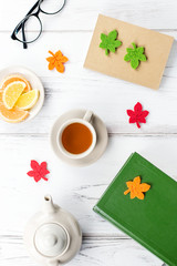 Feminine desk workspace flat lay with diary, eyeglasses, book, tea mug, sweets and felt decor.