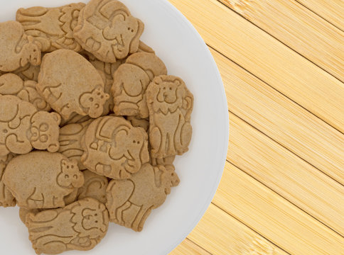Top close view of a plate of vanilla animal cookies on a wood place mat.